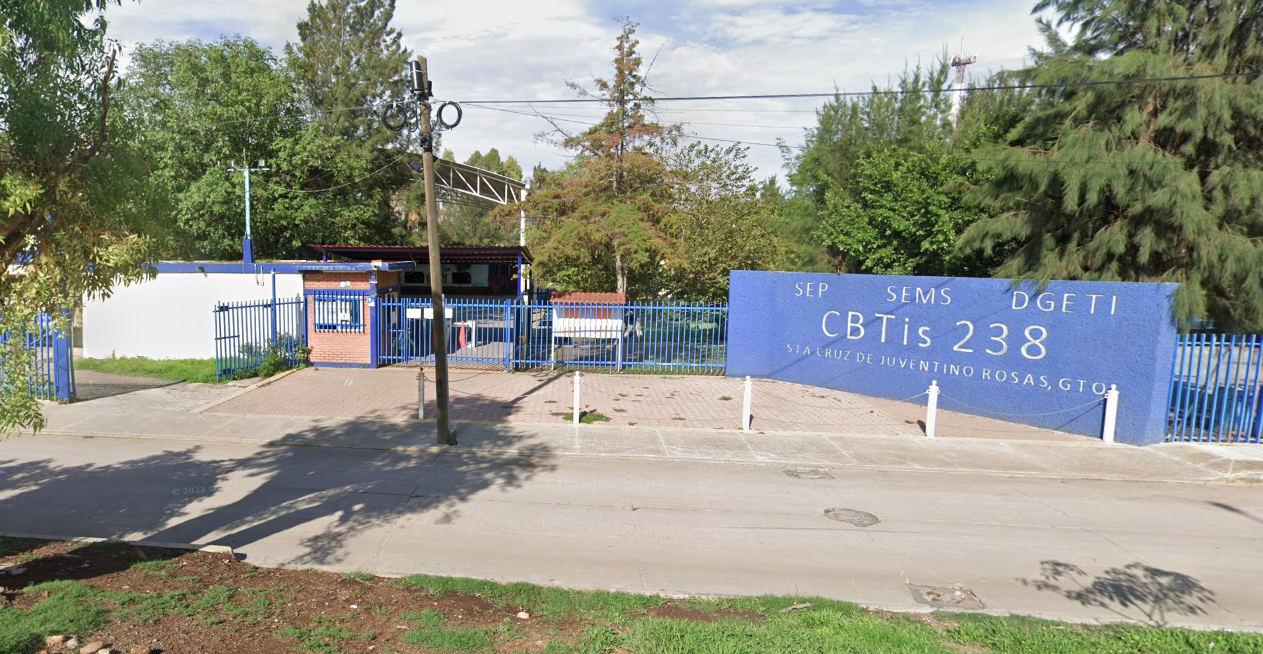 Fotografía en la que se muestra la entrada del plantel, conformada por una reja de color azul que rodea las instalaciones. Del lado derecho de la rej<a hay un muro azul que en letras blancas dice Cebetis 238.